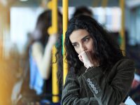 Pensive young woman traveling with bus and holding smart phone. Wears casual clothes.