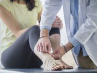 A young Asian woman is getting bandage wrapped around her foot by a male doctor inside a doctor's office. She is in a session for physical therapy.